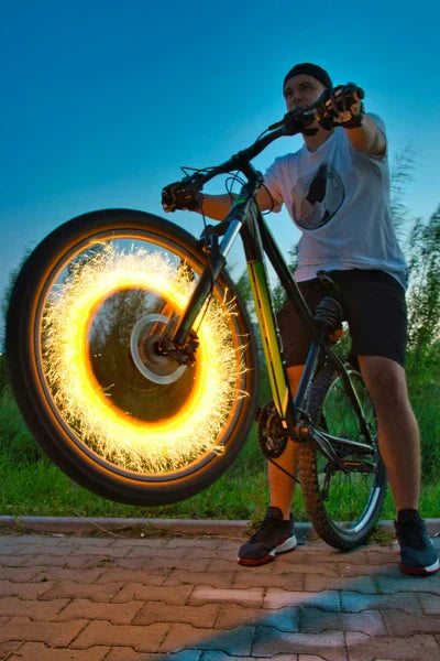 A man rides a bicycle with its wheel dramatically illuminated by a circular spark-like light effect