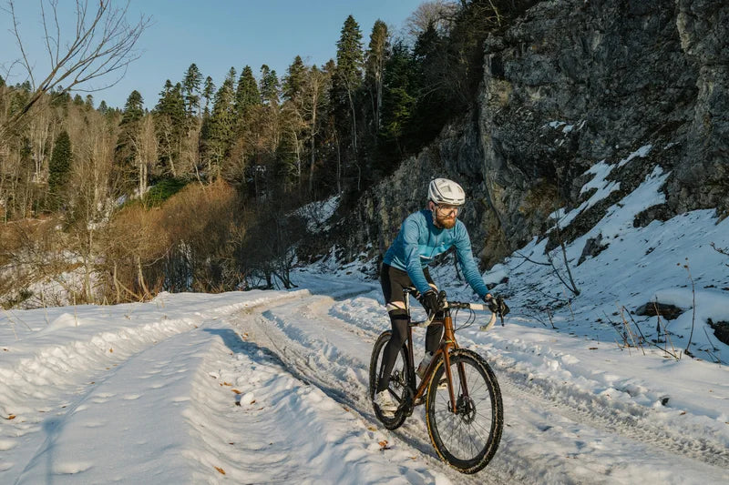 Man riding an electric bike on a snowy mountain trail under clear winter sunlight