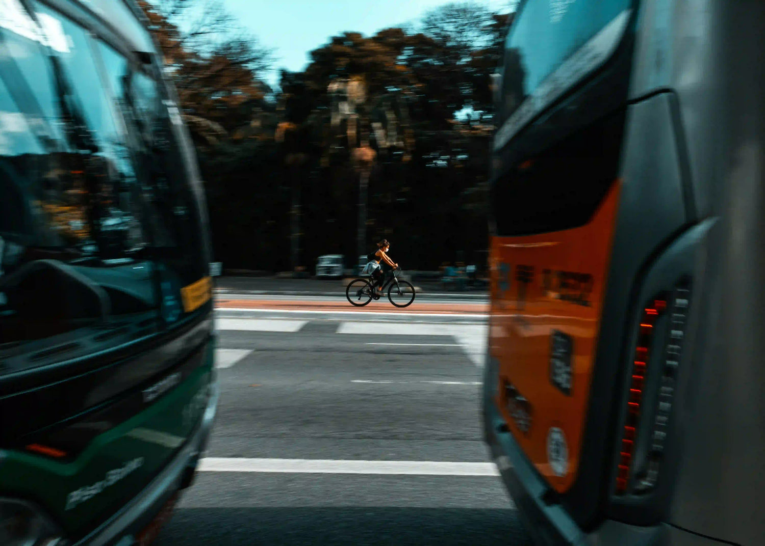 A cyclist riding quickly across a city street between two buses