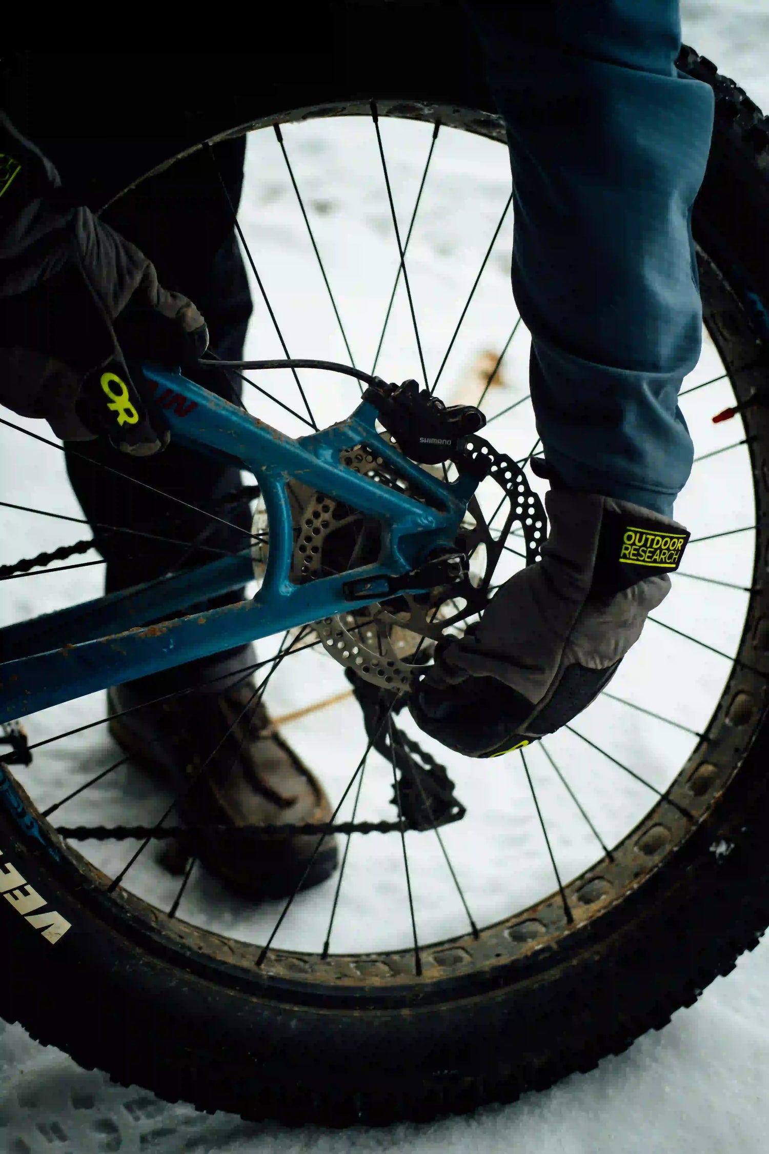 A person performing maintenance on a fat bike's disc brake in the snow.