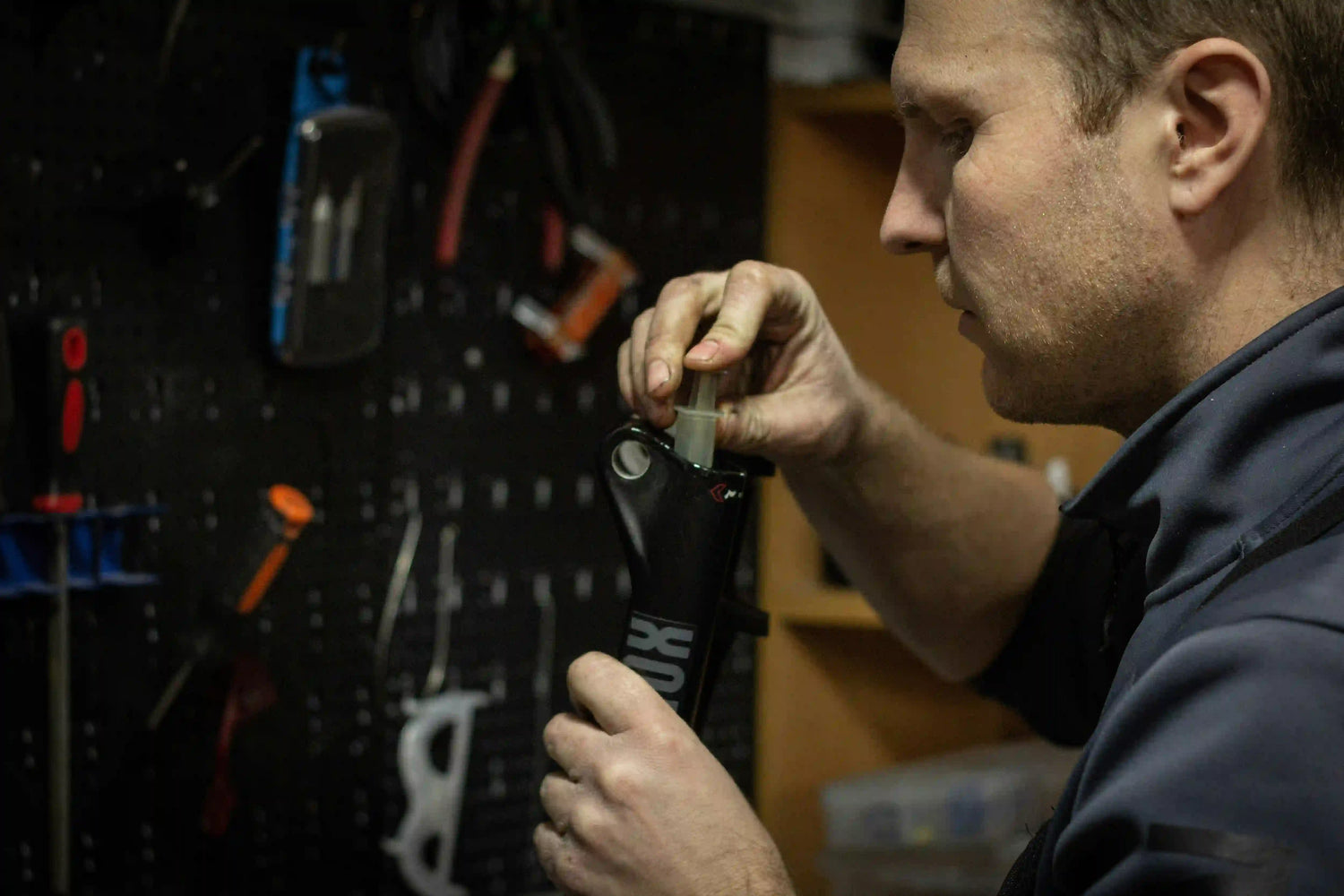 A focused bike mechanic servicing the internal components of a black suspension fork in a workshop.