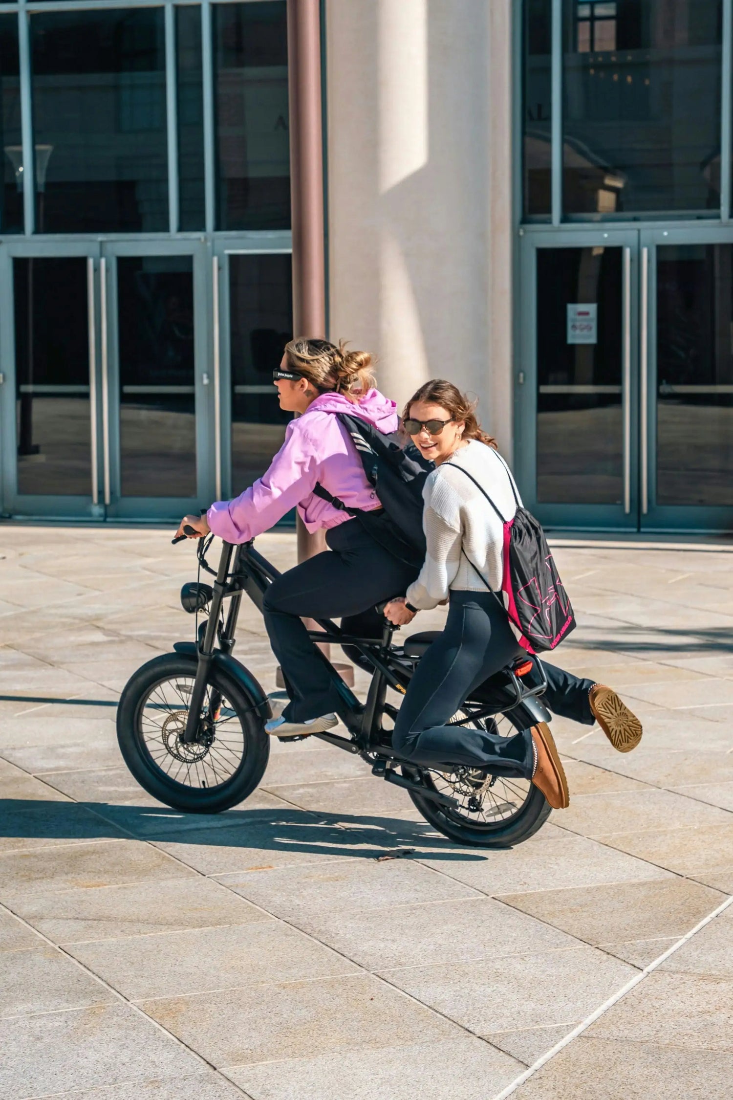 Two students riding together on a compact fatbike near campus buildings