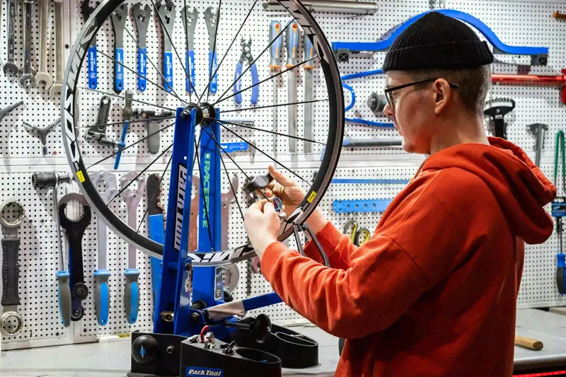 Professional bicycle mechanic truing a wheel in a fully equipped local bike shop, demonstrating the specialized service Lynxcle partners provide.